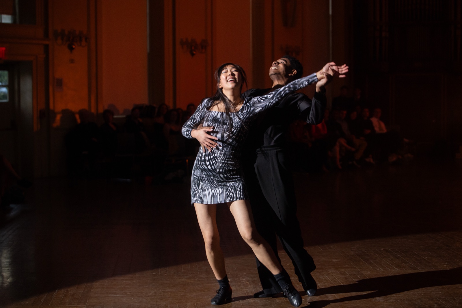 Two dancers in an arched line under a warm spotlight.