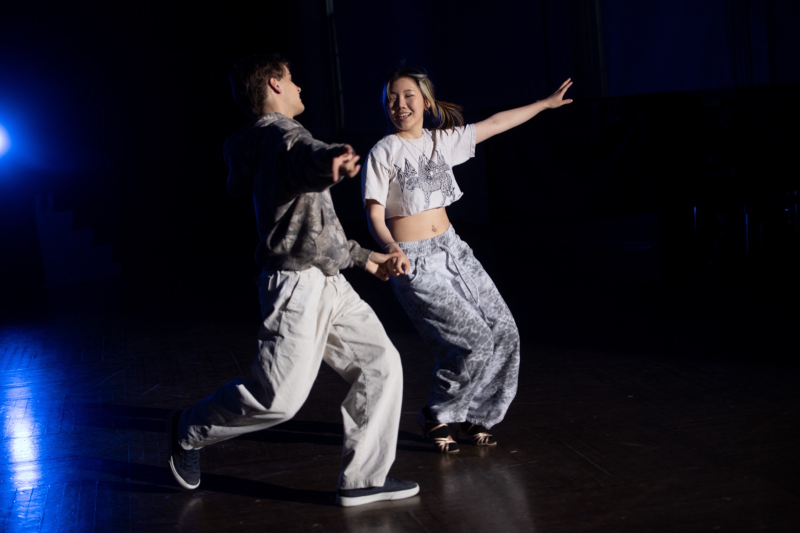 Two dancers in sweatshirts mid-lunge at a practice.