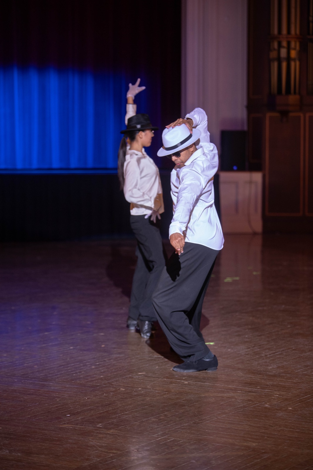 Two dancers in hats, lit against a blue curtain.